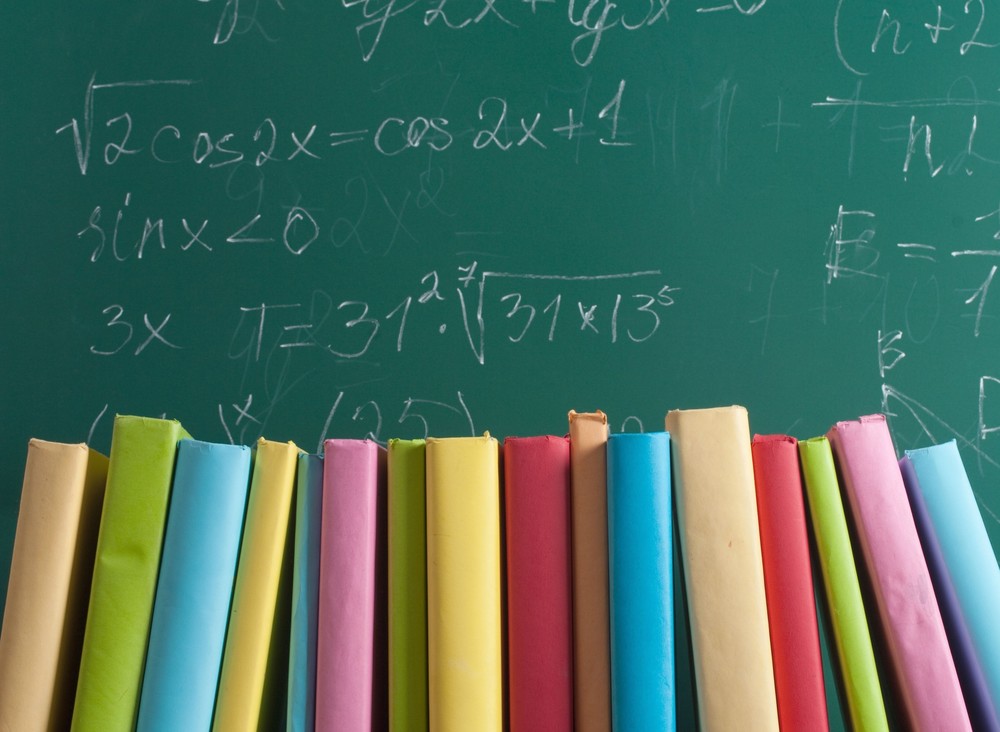 Books in front of chalkboard with various mathematical formulas written 